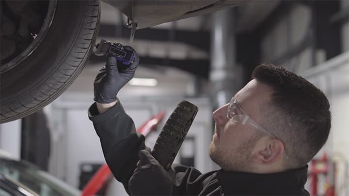 Vehicle technician checking over the tread depth of the tyre on a car