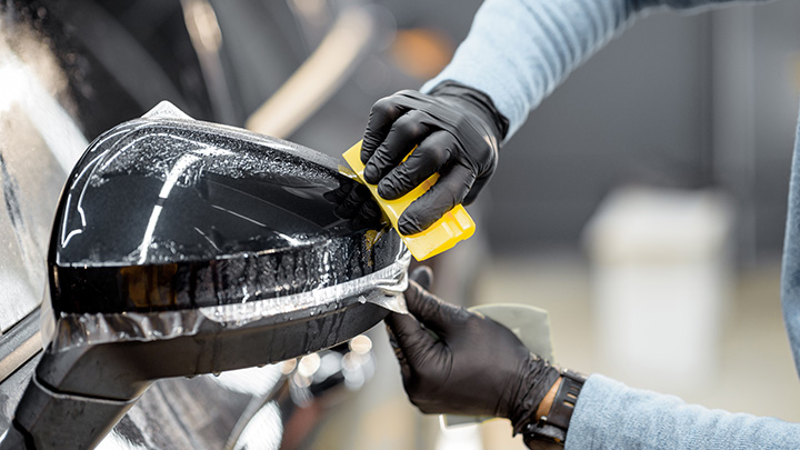 Paint protection film being applied to the side mirror of a car by a technician