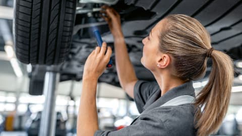 Female technician performing a visual inspection of a car's wheel