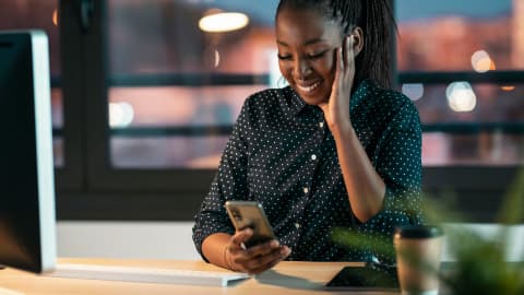A young female checking her phone whilst smiling and sitting at a desk