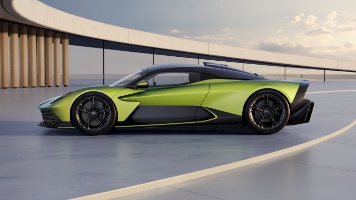 Side of a green Aston Martin Valhalla parked in a modern building with a grey sky in the background