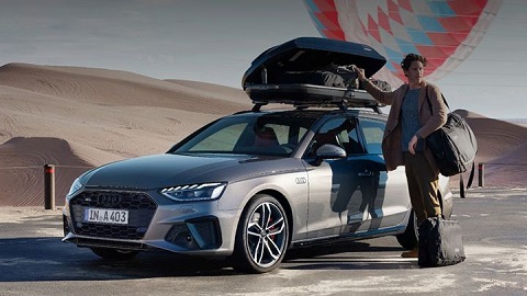 Lifestyle image of a man standing next to an Audi Avant with packed bags and a roof rack