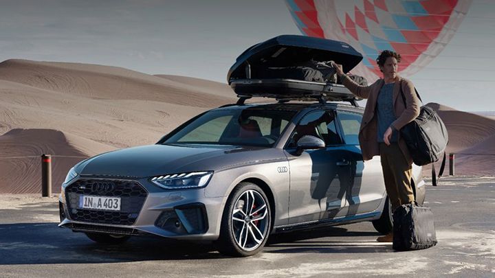 Lifestyle image of a man standing next to an Audi Avant with packed bags and a roof rack
