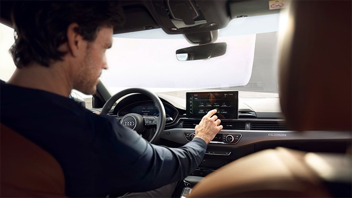 Over the shoulder shot of a young man using an Audi A4 Saloon's infotainment system