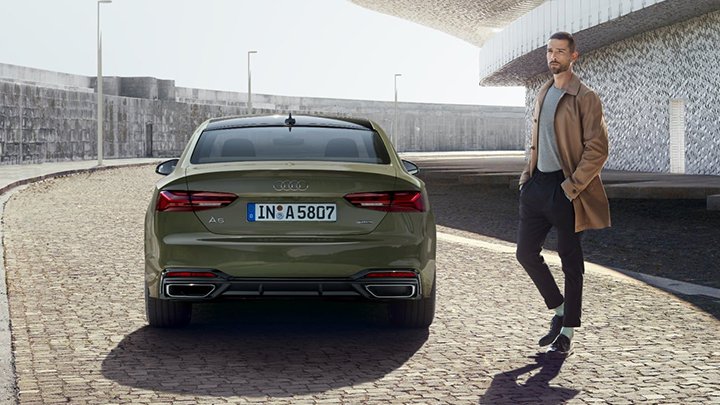 Stylish young man about to walk past the rear of a green Audi A5 Coupe
