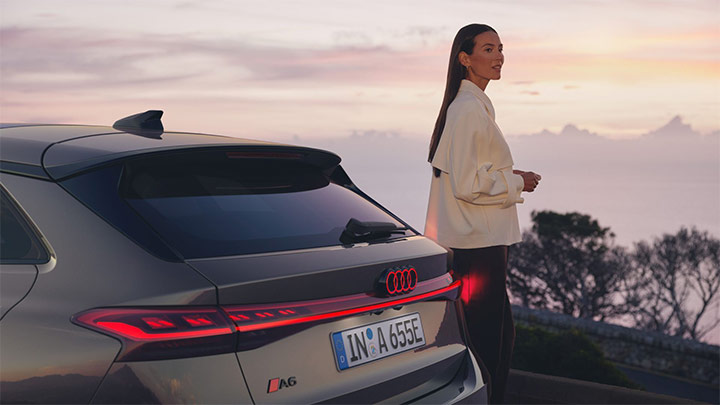 Young woman standing next to an Audi A6 Avant e-tron with a mountain background at dusk