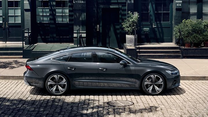 Side shot of a grey Audi A7 Sportback driving through a metropolitan setting