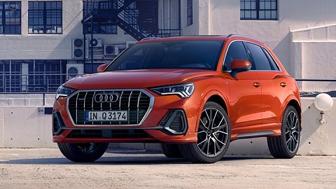 Front quarter shot of an orange Audi Q3 parked in front of a building