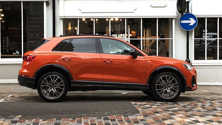 Side shot of an orange Audi Q3 driving past a shop