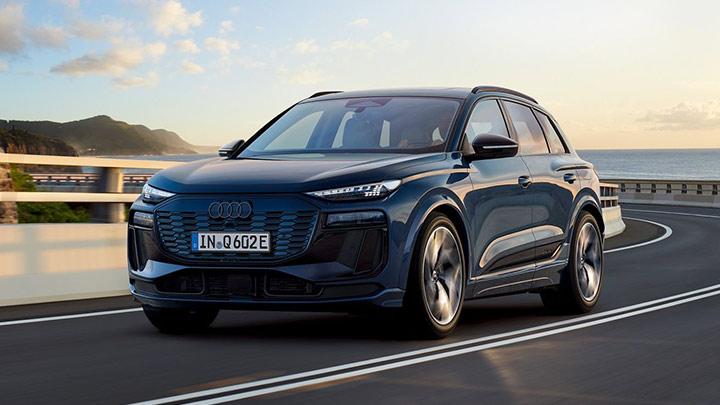 Front quarter shot of a blue Audi Q6 e-tron driving down a road at sunset