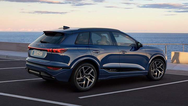 Side shot of a blue Audi Q6 e-tron parked in front of the ocean at sunset