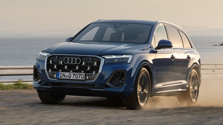 Front quarter shot of a blue Audi Q7 driving down a dusty road at sunset