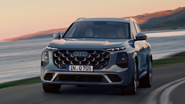 Audi Q7 SUV driving along coastal road at sunset, front three-quarter view
