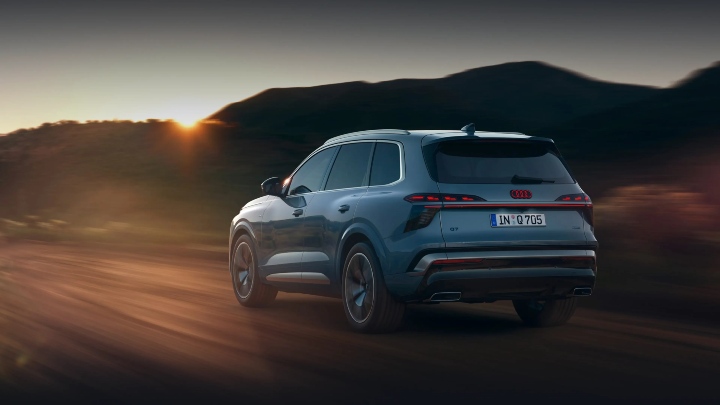 Audi Q7 driving on open road at sunset, rear three-quarter view