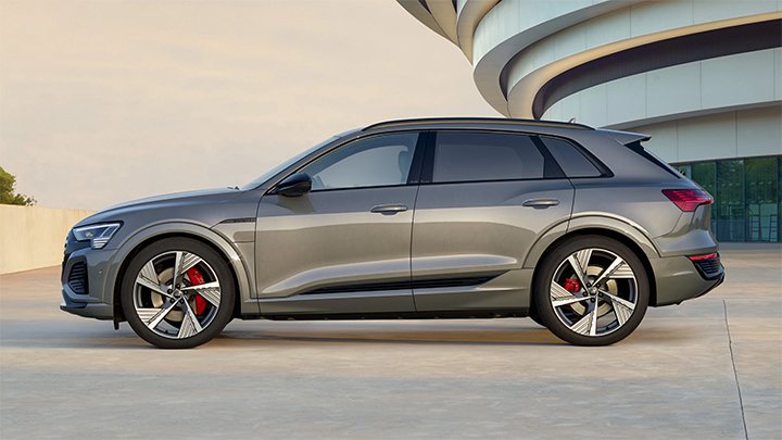 Side shot of a grey Audi Q8 parked in front of a modern arts building at sunset