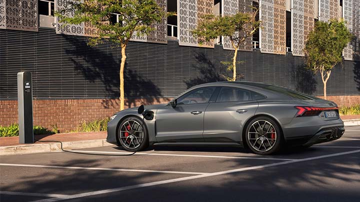 A grey Audi RS e-tron GT on charge in front of a modern building at sunset