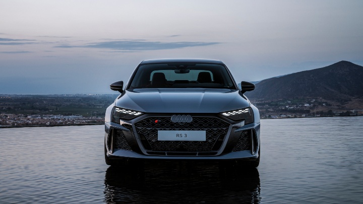 Front view of an Audi RS 3 Saloon beside a reflective waterside backdrop at dusk