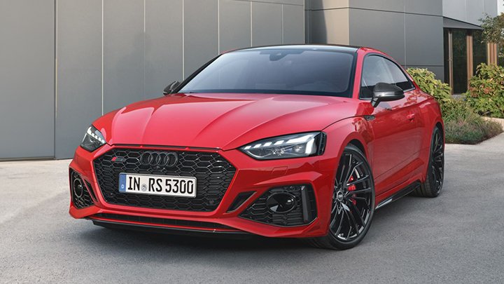 Front of red Audi RS5 Coupé parked in front of a grey wall with plants at the back