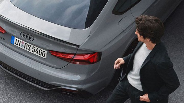 Man wearing a white shirt and black blazer walking behind a grey Aidu RS5 Sportback