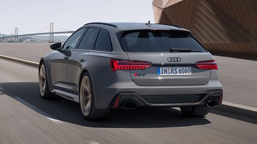 Back of a grey Audi RS6 Avant driving past a modern building with a large bridge and city ahead