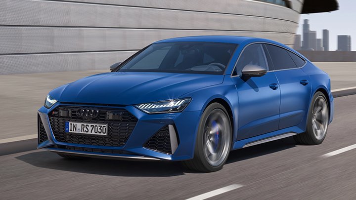 Blue Audi RS7 Sportback driving on a bridge with large skyscrapers on the background and a grey wall to its left side