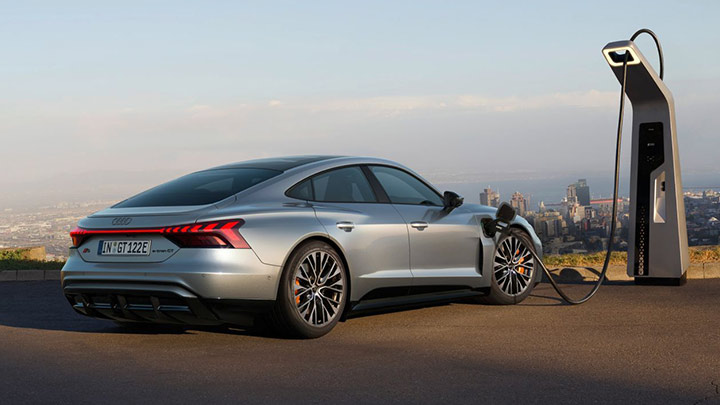 grey Audi S e-Tron GT parked in a mountain plugged into charger facing a large city below