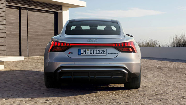 Back of grey Audi S e-Tron GT parked in front of a house with modern architecture and wooden garage doors