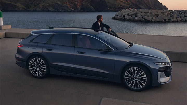 A man standing next to a blue Audi S6 Avant e-Tron with the door half open (pictured sideways) whilst observing the ocean and mountain horizon