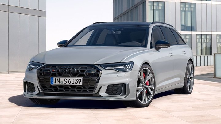 Front of a light grey Audi S6 Avant parked in front of a couple of metallic buildings