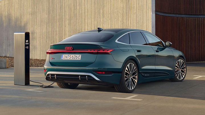 Back of a green Audi S6 Sportback e-Tron parked in front of a grey wall whilst being plugged in to the charger