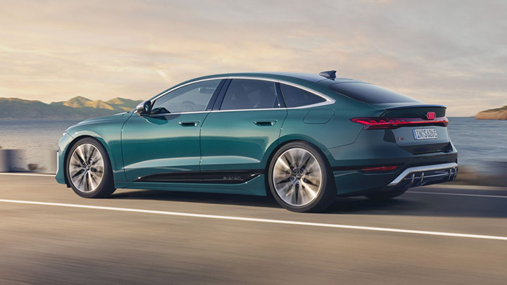 Side of a blue S6 Sportback e-Tron driving by the ocean with mountains in the background