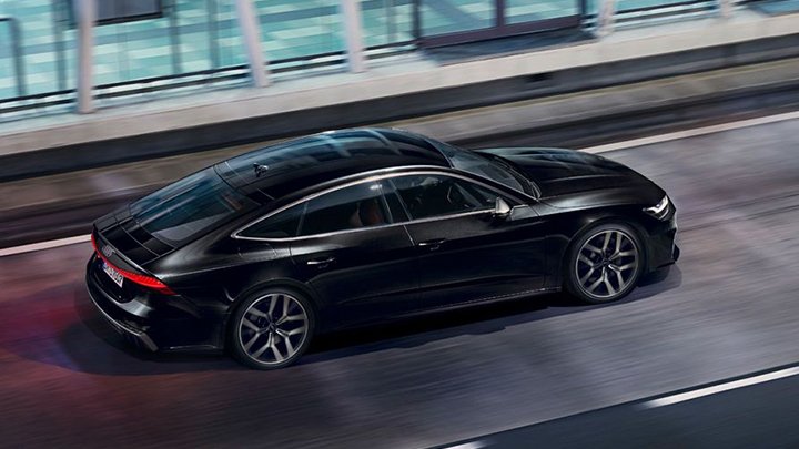 Roof of a black Audi S7 Sportback driving on an asphalted road with a large building with glass walls on the side