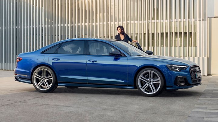Woman wearing a black top getting in a blue Audi S8 parked sideways in front of a metallic wall with small gaps between them