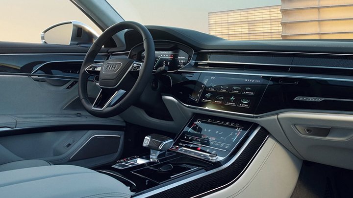 Cabin of an Audi S8 where you can see the steering wheel, the infotainment system and grey seats