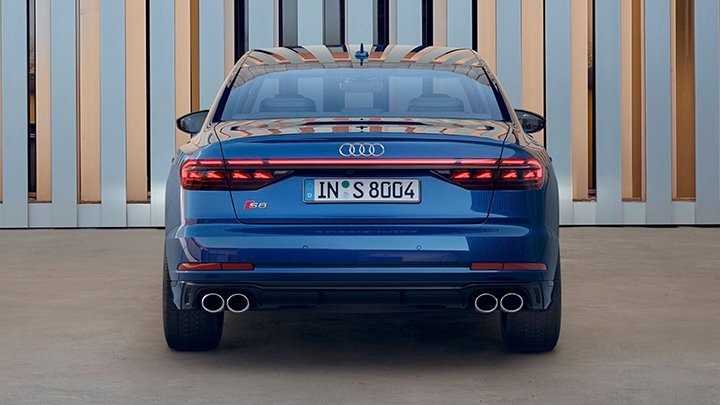 Back of blue Audi parked in front of a metallic gate with small gaps that reveal a beige wall inside