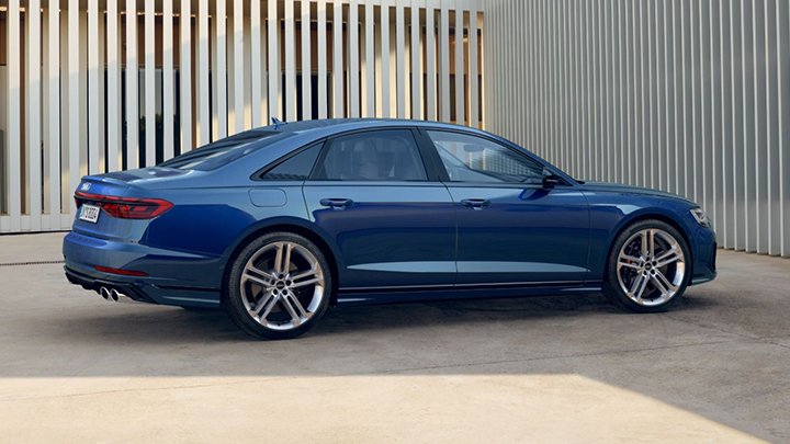 Side of a blue Audi S8 parked in front of a metallic gate with small gaps that reveal a wall inside