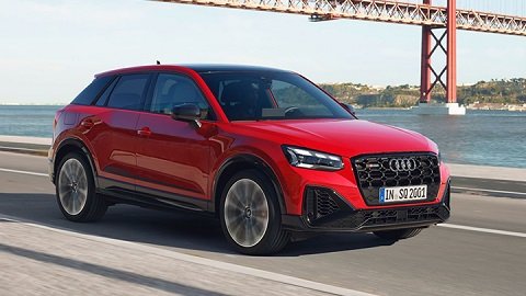 Red Audi SQ2 driving on a road besides a large river with blue water (that can be seen in the background) and a large bridge with copper detailing and mountains can be seen behind the car