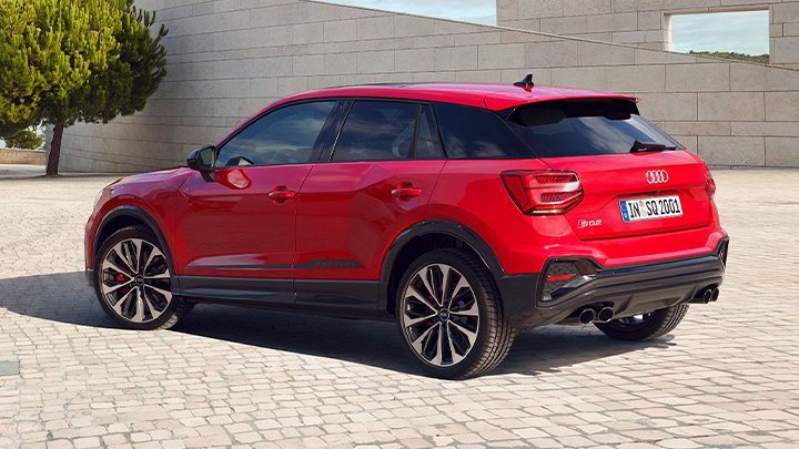 Back of red Audi SQ2 parked in front of a stone wall with a tree in front of it