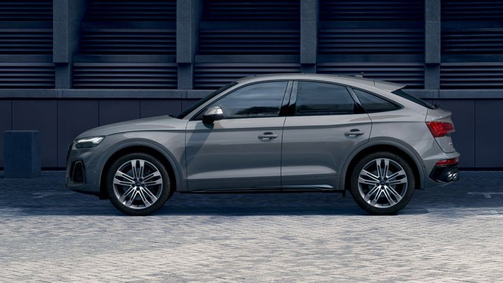 Side of grey SQ5 Sportback parked in front of a grey building with large windows separated by concrete details
