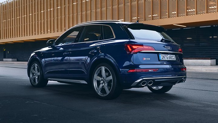 Rear of navy blue Audi SQ5 driving in the city with a modern building in the background