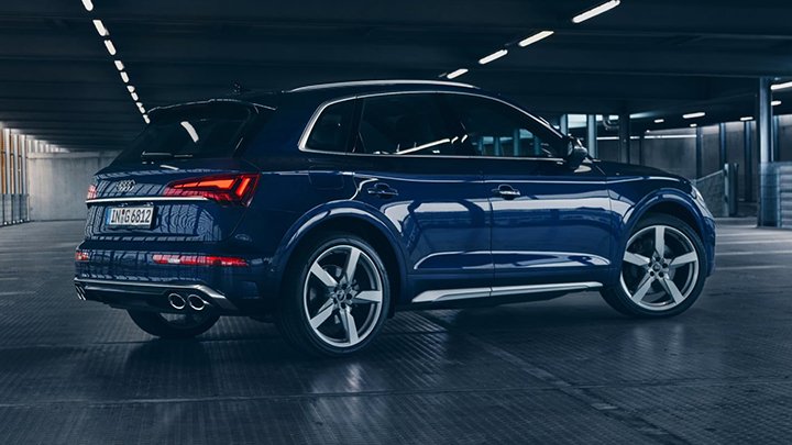 Side and rear of navy blue Audi SQ5 parked in a dark car park with black flooring and concreate walls