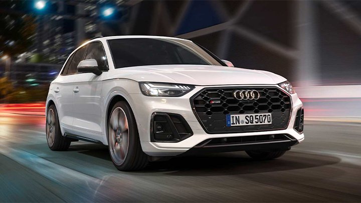 White Audi SQ5 driving in the city with large buildings in the background