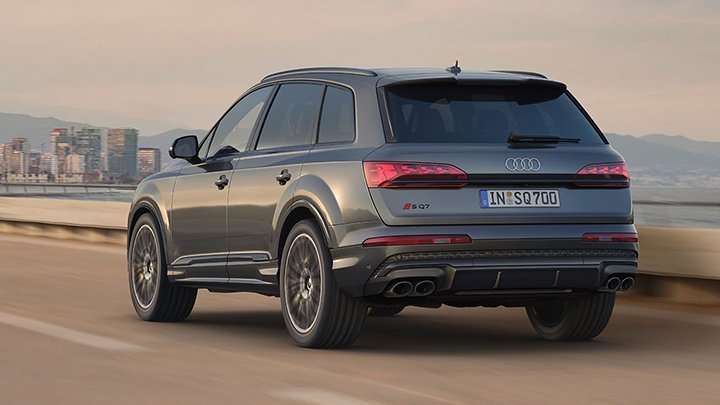 Bakc of grey Audi SQ7 Sportback driving in a mountain with a city ahead where mug skyscrapers can be seen in the background
