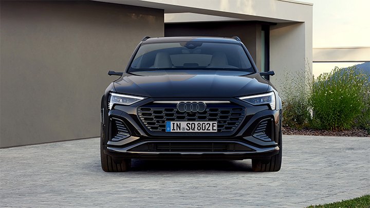 Front of black Audi SQ8 e-Tron parked in front of a house with modern architecture and beige walls. 
