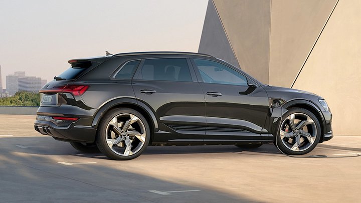 Side of a black Audi SQ8 e-Tron parked in front of a modern building with beige walls