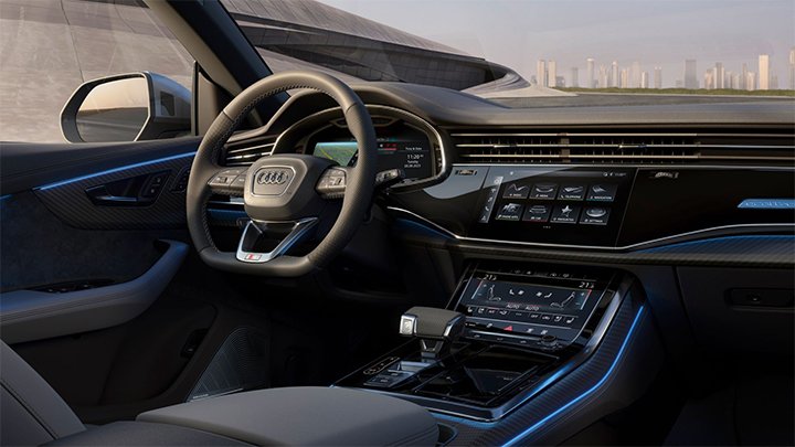 Cabin of an Audi SQ8 where you can see the steering wheel, the infotainment system and dark grey seats