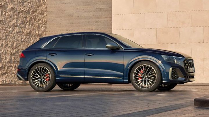 Blue Audi SQ8 is parked sideways in front of a tall stone wall coloured beige