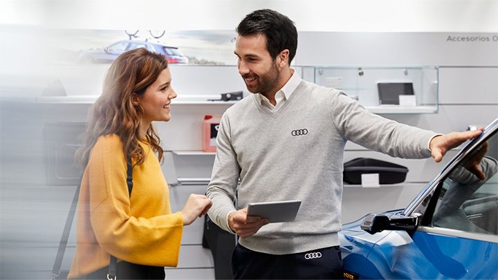 A service advisor running through a car service with a young woman standing next to a blue Audi