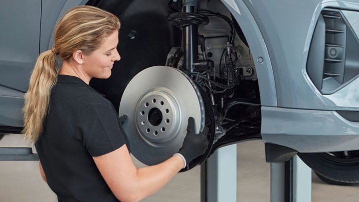 A young woman working on the front brakes of an Audi