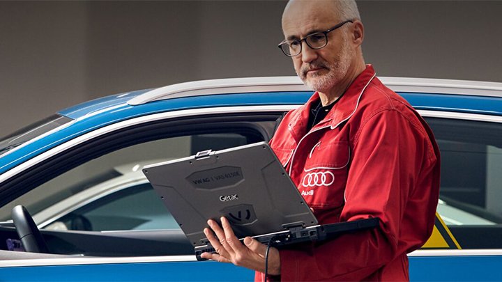 Audi technician standing in front of a blue Audi whilst looking at a laptop